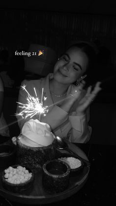 a woman sitting in front of a cake with white frosting and sparklers on it