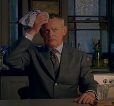 a man in a suit sitting at a table with a drink and napkin over his head