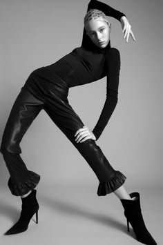 a woman in black is posing with her legs spread out and wearing high heeled boots