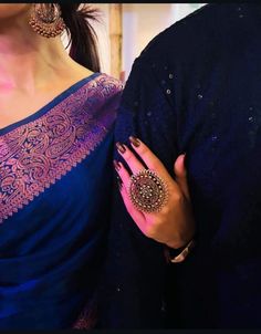 a woman in a blue sari and matching ring stands next to a man wearing a black jacket