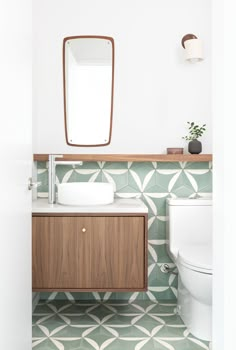 a white toilet sitting next to a wooden cabinet in a bathroom under a mirror above a sink