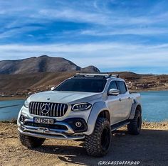 a white mercedes benz truck parked on the side of a road next to a body of water