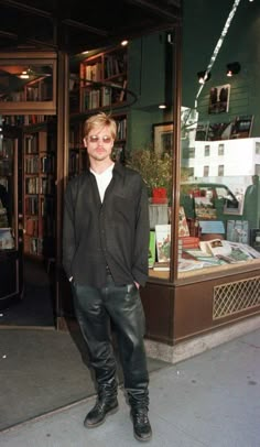 a man standing in front of a book store wearing black leather pants and knee high boots