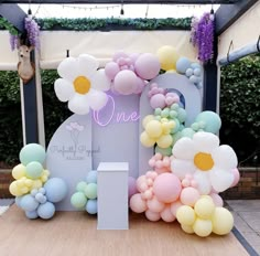 an outdoor event with balloons and flowers on the stage for a one year birthday party