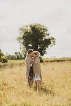 two people standing in the middle of a field hugging each other and smiling at one another