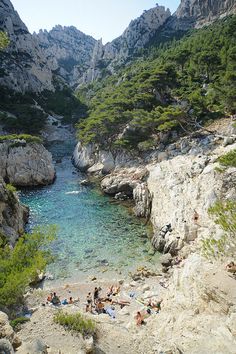 some people are swimming in the water near rocks and trees, while others rest on the beach