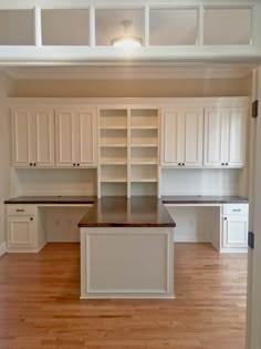 an empty kitchen with white cabinets and wood floors