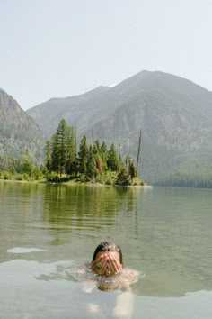 a person swimming in a lake with mountains in the background and trees on both sides