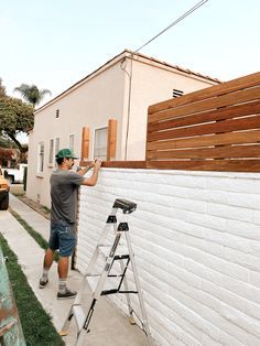 a man is painting the side of a white brick building with wood slats on it