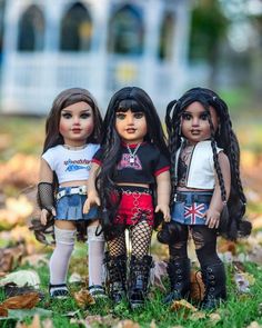 three dolls are standing next to each other in the grass with leaves on the ground