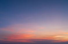 an airplane flying in the sky at sunset with clouds and water behind it, as seen from across the ocean