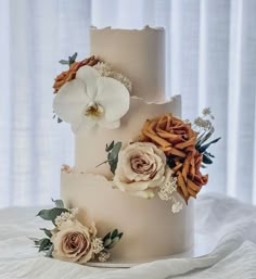 a three tiered wedding cake with flowers on the top and bottom, sitting on a white tablecloth