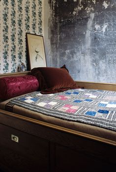 a bed with a quilt on top of it in a room that has wallpaper