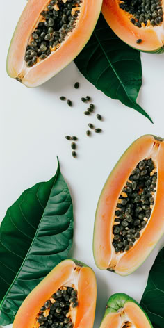 papaya slices with seeds and leaves on a white surface