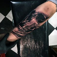 a man's arm with a black and grey tattoo on it, which has a skull in the middle