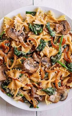 a white bowl filled with pasta and spinach on top of a wooden table next to a fork