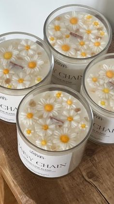 four candles with daisies in them sitting on a wooden table next to each other