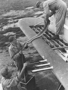 men working on an airplane in the middle of a field with another man standing next to it