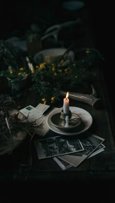 a lit candle sitting on top of a table next to pictures and flowers in the dark