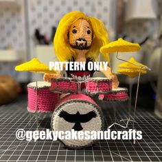 a crocheted doll sitting on top of a pink drum set with yellow drums