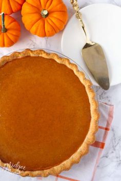 a pumpkin pie sitting on top of a table next to two small orange pumpkins