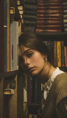 a woman leaning against a bookshelf with her head on the book shelf and looking at the camera