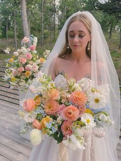 a woman in a wedding dress holding a bridal bouquet on a wooden deck with trees in the background