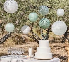 a table topped with a white cake and lots of paper lanterns hanging from the trees