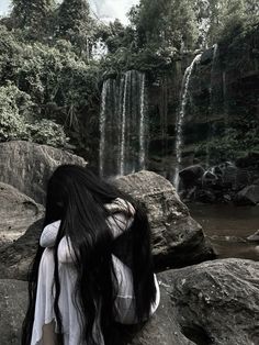 a woman with long black hair standing in front of a waterfall