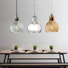 three glass pendant lights hanging over a table with wine glasses and plates on the table