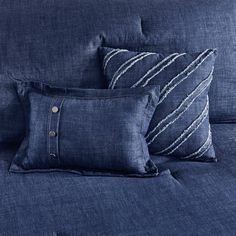 two blue pillows sitting on top of a bed next to a pillow case with buttons