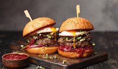 two hamburgers with meat and cheese on a cutting board