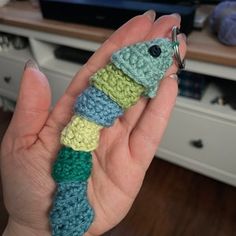 a hand holding a crocheted keychain in front of a tv