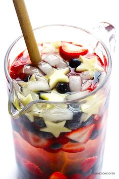 a glass filled with fruit and ice sitting on top of a table next to a wooden spoon