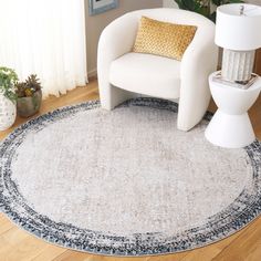 a white chair sitting on top of a wooden floor next to a rug and lamp