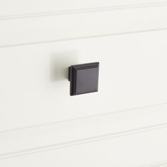 a black square knob on a white cabinet