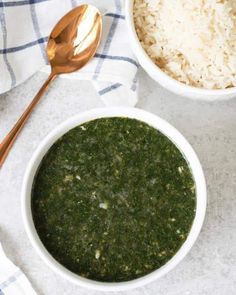 two white bowls filled with green food next to a spoon and bowl of rice on a table