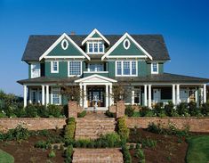 a large green house with white trim on the front and side windows, surrounded by greenery