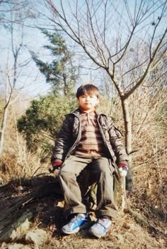 a young man sitting on top of a tree stump