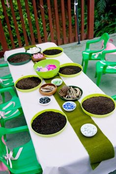 a table topped with bowls filled with dirt next to green chairs and tables covered in plates