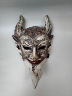 a white mask with horns is hanging on the wall