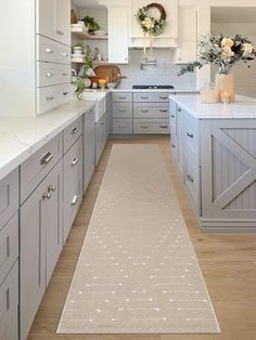 a long narrow kitchen with white cabinets and wood flooring, along with a beige runner rug