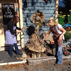 two women are decorating a scarecrow in front of a store