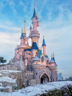 the castle is pink and blue with gold spires on it's roof, surrounded by snow