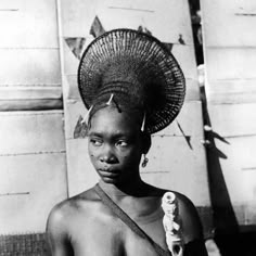 a woman with a hat on her head standing in front of a building and looking at the camera