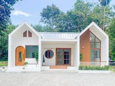 a white house with wooden doors and windows in the front yard, surrounded by trees