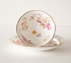 an empty tea cup and saucer on a white surface with pink, yellow and green flowers