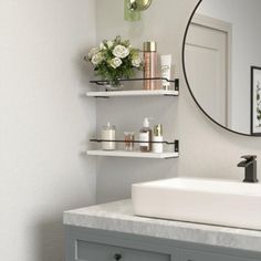 a bathroom sink sitting under a mirror next to a shelf with candles and flowers on it