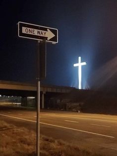 a one way street sign in front of a cross on the side of a road