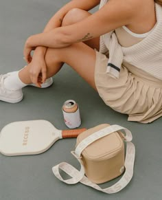 a woman sitting on the ground next to her purse and other items including a bottle